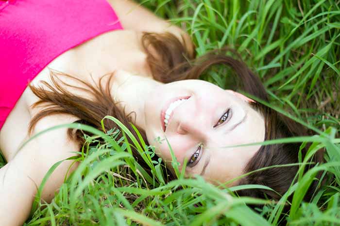 Mujer sonriente tumbada sobre césped natural.